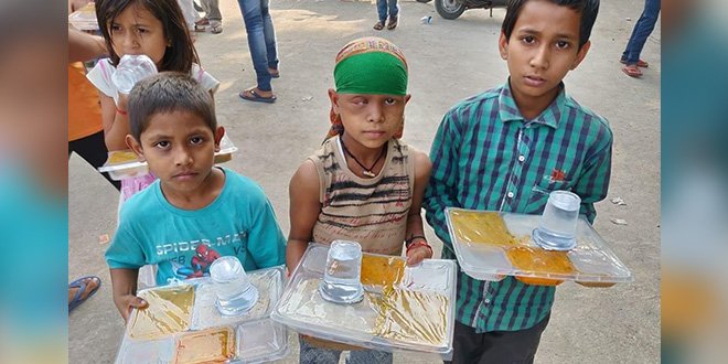 Three children holding food and drink trays outdoors, looking at the camera