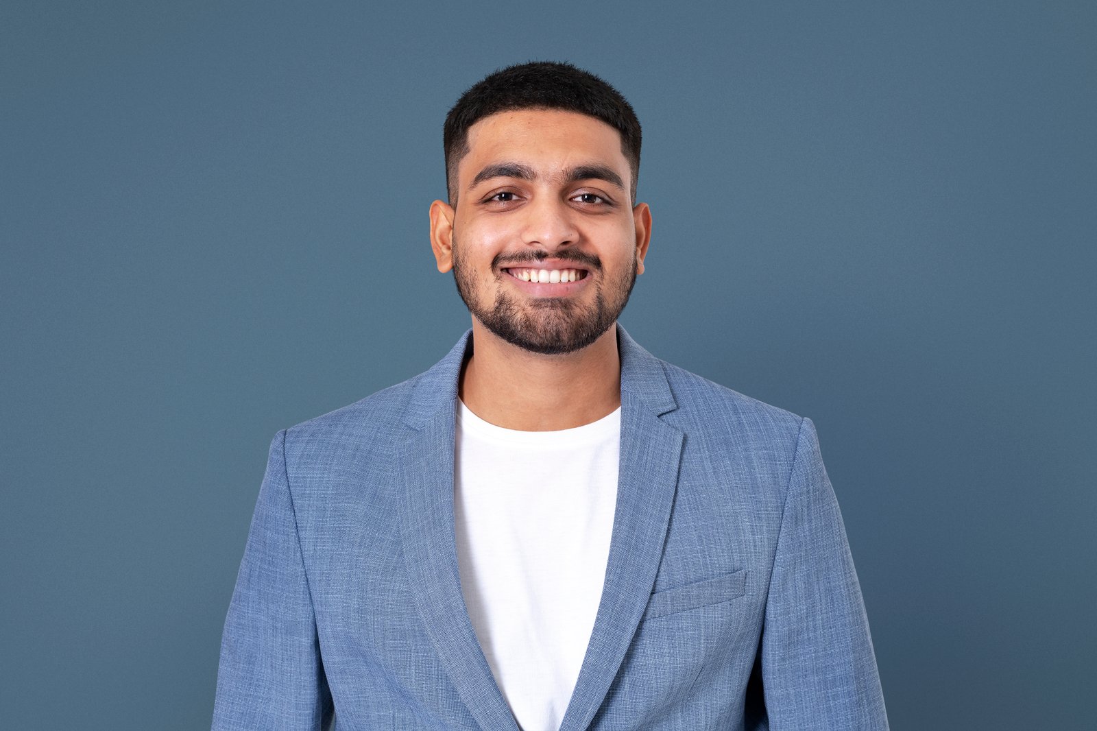 Smiling man in light blue blazer and white shirt against gray background