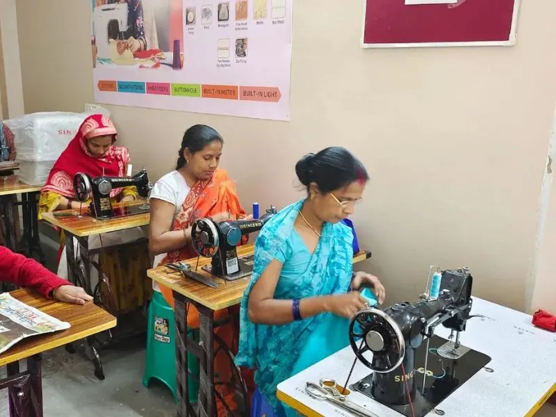 Women sewing fabric at tables in a small workshop classroom