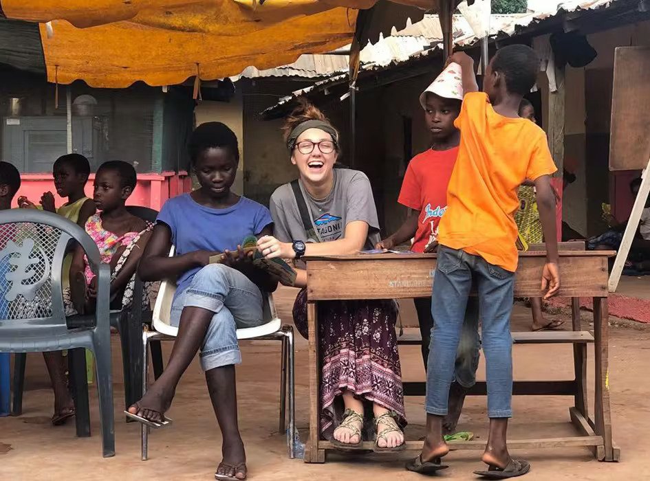 Group seated under a canopy, with one man in an orange shirt standing nearby.